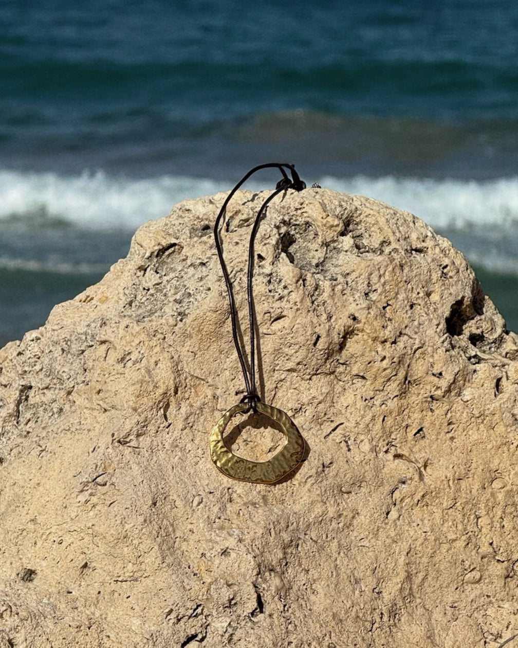 Handmade Aegean Necklace featuring hammered gold or silver pendant on adjustable black or brown leather cord, with optional hand-wrapped gemstone.