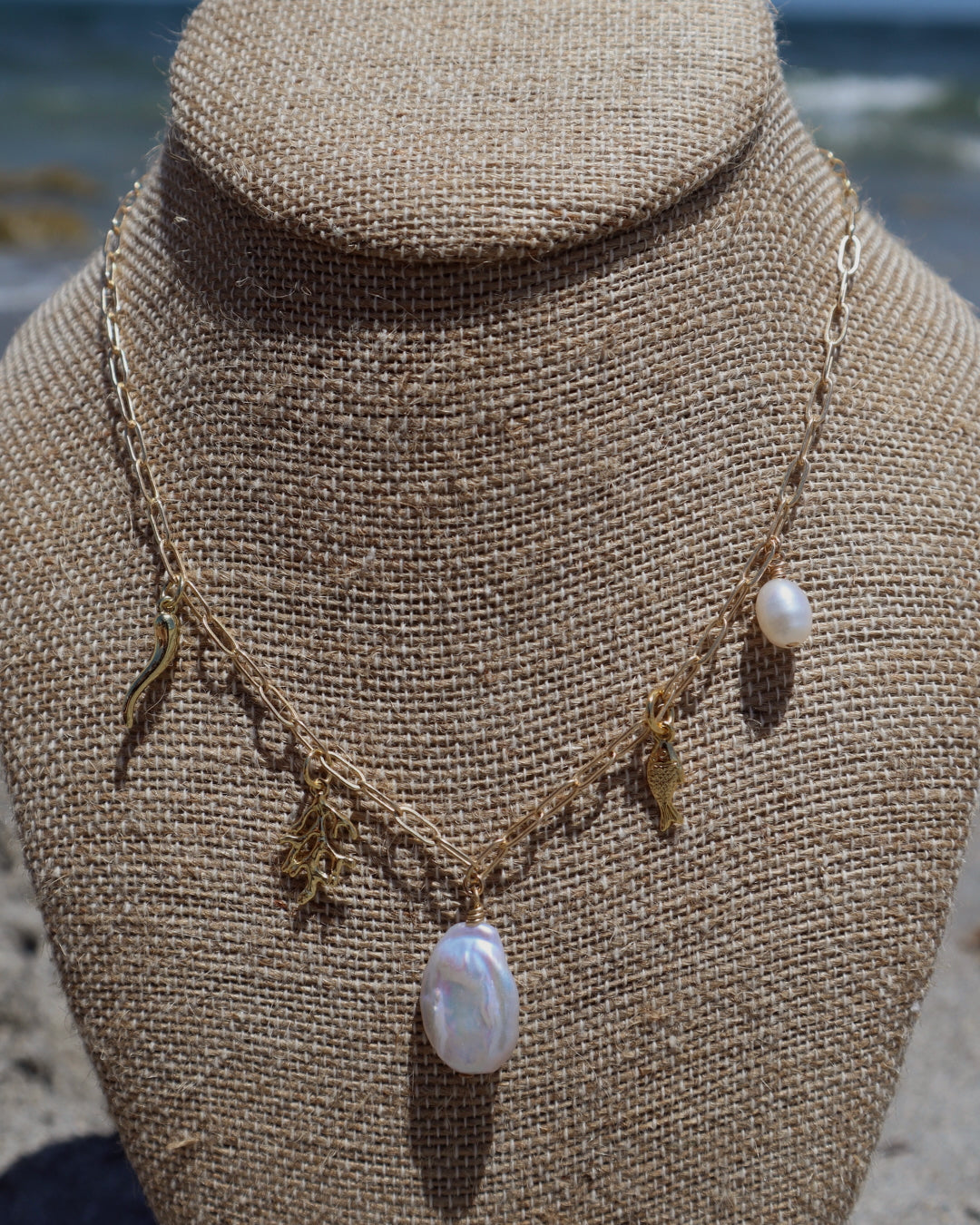 Handmade Indie Mare Charm Necklace featuring freshwater pearls, coral, gold-plated fish, and Italian horn charms on a gold-filled chain, ocean-inspired.