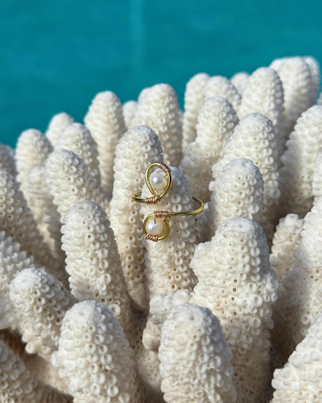 Gold ring with pearl on a piece of coral with turquoise water in the background
