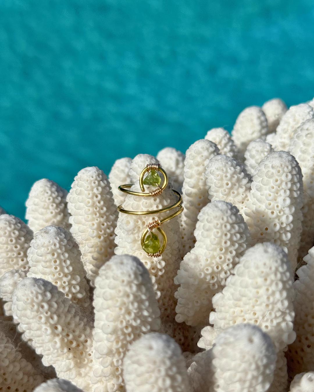 Gold ring with a Peridot gemstone on a piece of coral with a blue water background